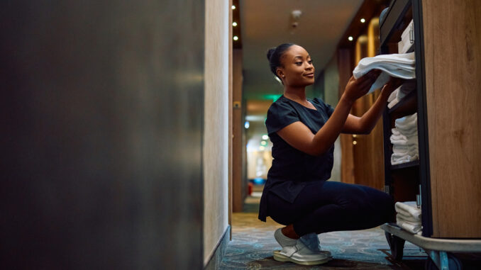 Young black maid taking clean towels from a cart while working in a hotel.
