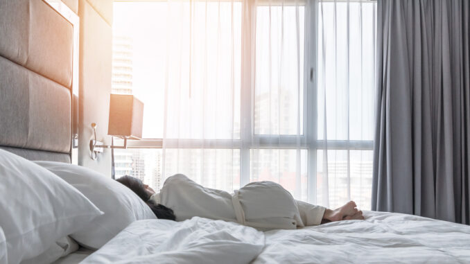 Sleeping in hotel bed with good rest of young woman lifestyle lying in bedroom relaxing waking up late in the morning for world lazy day concept